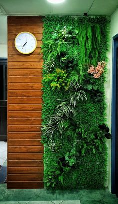 a clock is on the side of a green wall that has plants growing on it