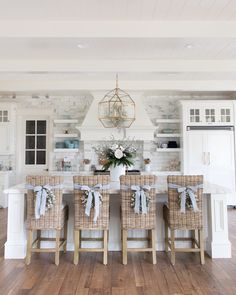 a kitchen with white walls and wooden floors, decorated in wicker chairs at the center island