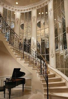 a grand piano sitting in front of a staircase with glass doors and windows on the wall