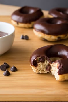 chocolate covered doughnuts sitting on top of a wooden cutting board next to a bowl of chocolate chips