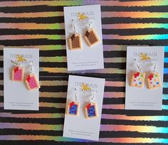 three earrings are shown on top of a card and in front of a rainbow background