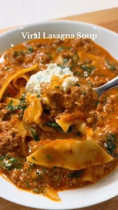 a white bowl filled with pasta and meat sauce on top of a wooden table next to a spoon