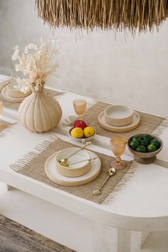 the table is set with plates, bowls and fruit in vases next to it