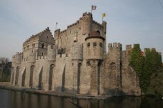 an old castle sitting next to a body of water with flags on it's sides