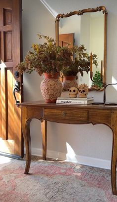 a wooden table topped with a vase filled with flowers next to a mirror and door