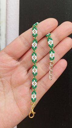 a hand holding a green and white beaded bracelet on it's left side