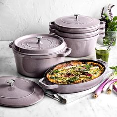 several pots and pans are sitting on a table next to some vegetables, including an onion