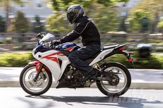 a man riding on the back of a white motorcycle down a street next to trees