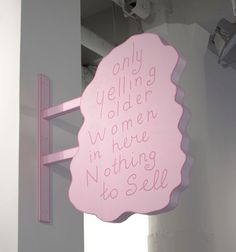 a pink sign hanging from the side of a white wall next to a window with writing on it