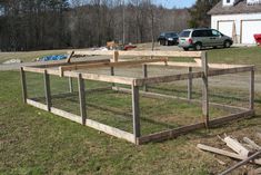 an animal pen in the middle of a yard next to a house with cars parked nearby