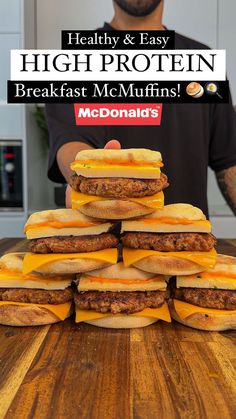 a stack of hamburgers sitting on top of a wooden table next to a man