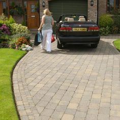 a woman walking towards a black car in front of a house with a red bag