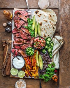 an assortment of meats and vegetables on a plate with pita bread, avocado, salsa, lime wedges