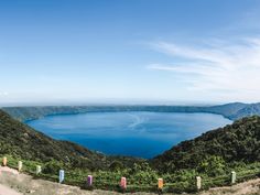 a large body of water surrounded by green hills and trees on a sunny day with blue sky