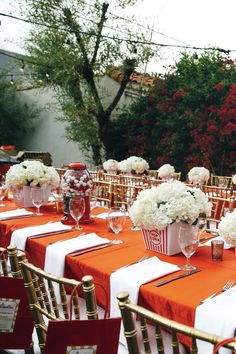 an outdoor wedding reception set up with orange linens and white flowers in vases