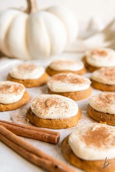 pumpkin spiced cookies and cinnamon sticks are arranged on a baking sheet with white pumpkins in the background