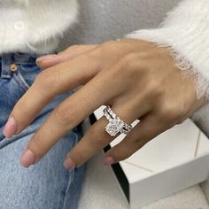 a woman's hand wearing a ring with two diamonds on it, sitting in front of a white box