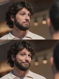 a man with curly hair and beard wearing a white sweater looks at another man's face