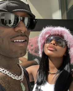 a man wearing sunglasses and a pink hat next to a woman