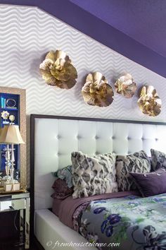 a bedroom with purple walls and gold flowers on the headboard, along with decorative wall hangings