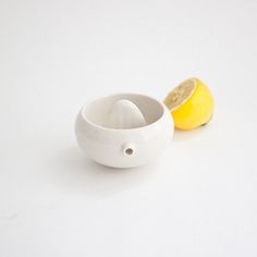 a white bowl with a lemon in it and a piece of fruit next to it