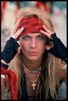 a woman with long blonde hair wearing a red bandana and black gloves on her head