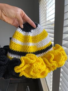 a hand holding a yellow and black knitted hat