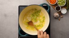 a person stirring vegetables in a pot on top of an electric burner with a wooden spoon