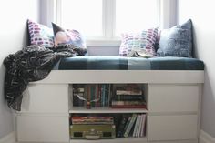 a window seat with books on it in front of a book shelf filled with books