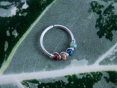 a close up of a ring on a leaf with three beads hanging from it's end