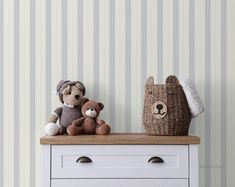 two teddy bears sitting on top of a dresser next to a basket and wallpaper