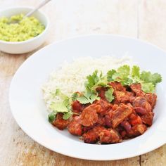 a white plate topped with meat and rice next to a bowl of guacamole