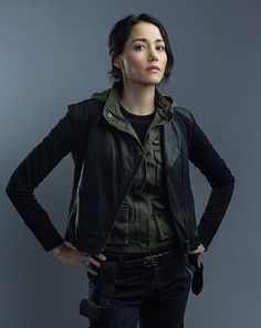 a woman in black leather jacket standing with her hands on her hips and looking to the side