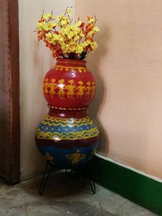 a red vase with yellow flowers in it sitting on a stand next to a wall