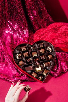 a heart shaped box filled with chocolates sitting on top of a pink table cloth