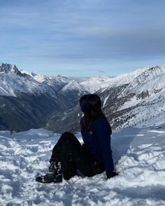 a woman sitting in the snow on top of a mountain looking at mountains and valleys