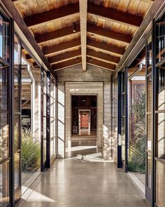 an empty hallway with glass doors leading to another room and the ceiling is made of wood