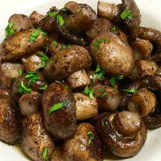 a white bowl filled with cooked mushrooms and parsley