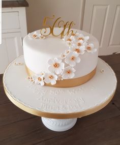 there is a white cake with gold trim and flowers on the top that says 50th