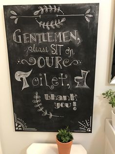 a chalkboard on the wall above a toilet with a potted plant next to it