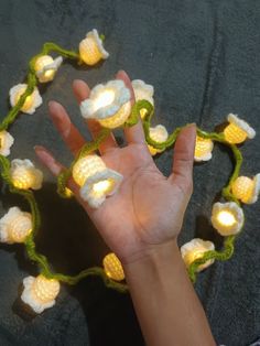 a person's hand is shown with crocheted flowers on it, and there are lights in the background