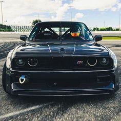 the front end of a black sports car driving on a track with clouds in the background