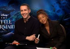 a man and woman sitting next to each other in front of a sign that says the little mermaid