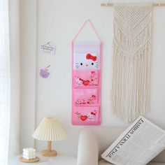 a pink hello kitty hanging on the wall next to a lamp and a magazine rack