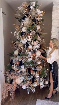 a woman decorating a christmas tree in her living room with white and gold decorations