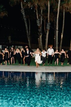 a group of people standing next to each other near a pool in front of palm trees