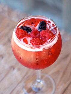 a close up of a drink in a glass on a wooden table with berries and ice