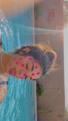 a woman with pink flowers on her face standing next to a pool