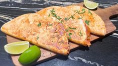 three quesadillas on a cutting board with limes