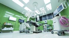 an operating room with green tile walls and ceiling lights, equipment on the floor, and overhead lighting